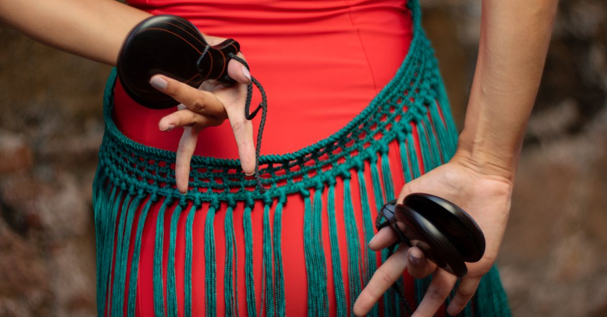 A close-up of a dancer's hands holding castanets with a colorful costume detail.